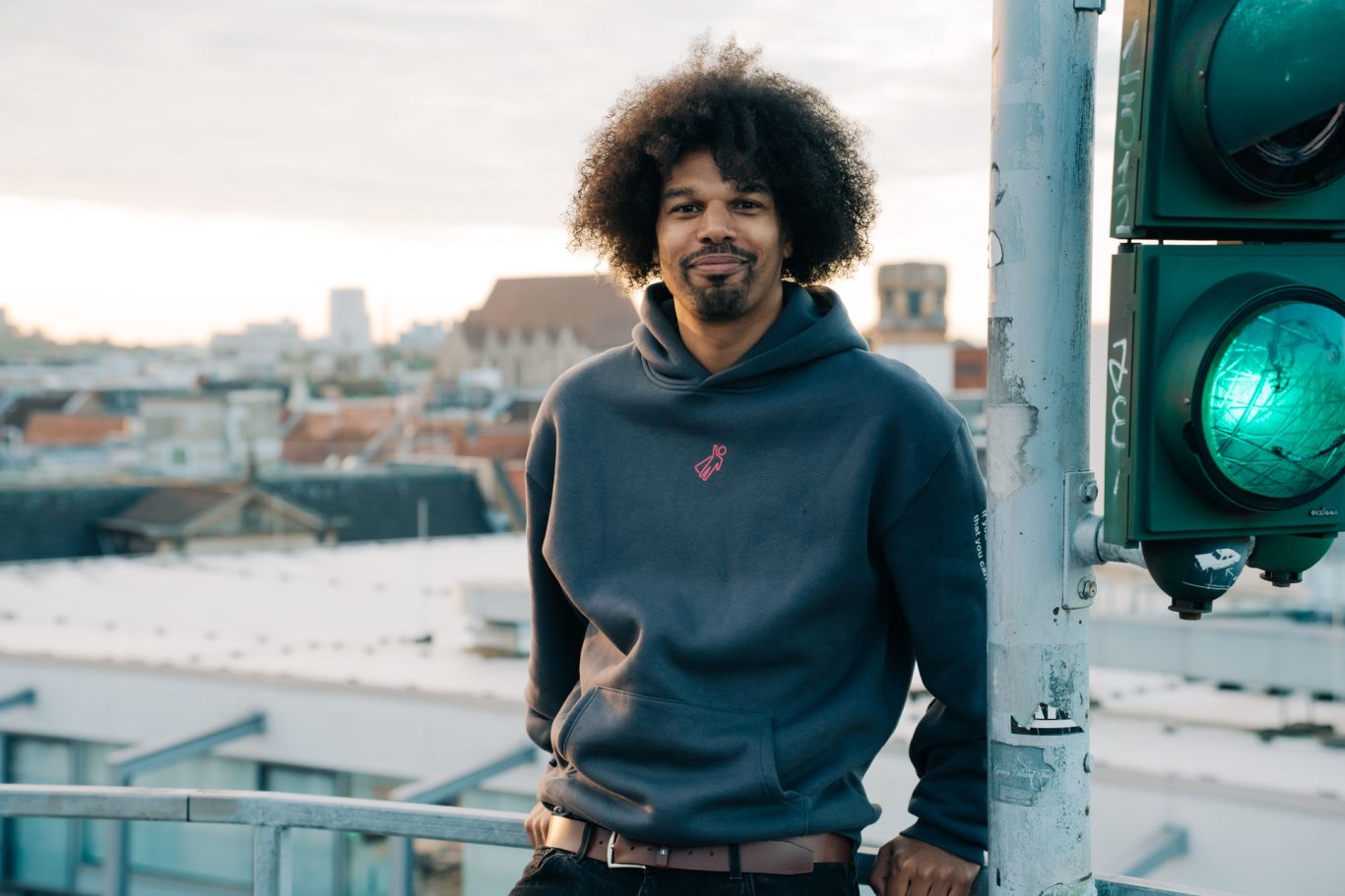 Mann mit lockigem Haar steht vor einer grünen Ampel und Blick auf die Stadt.
